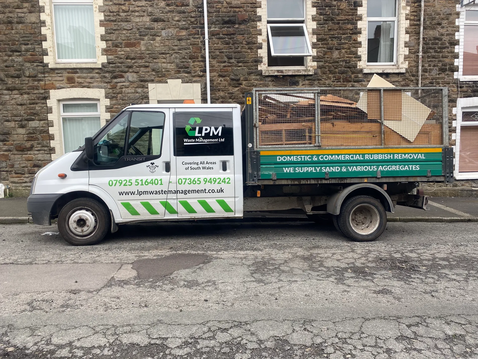 a photo of a waste truck outside on the roadside in front of a stone house