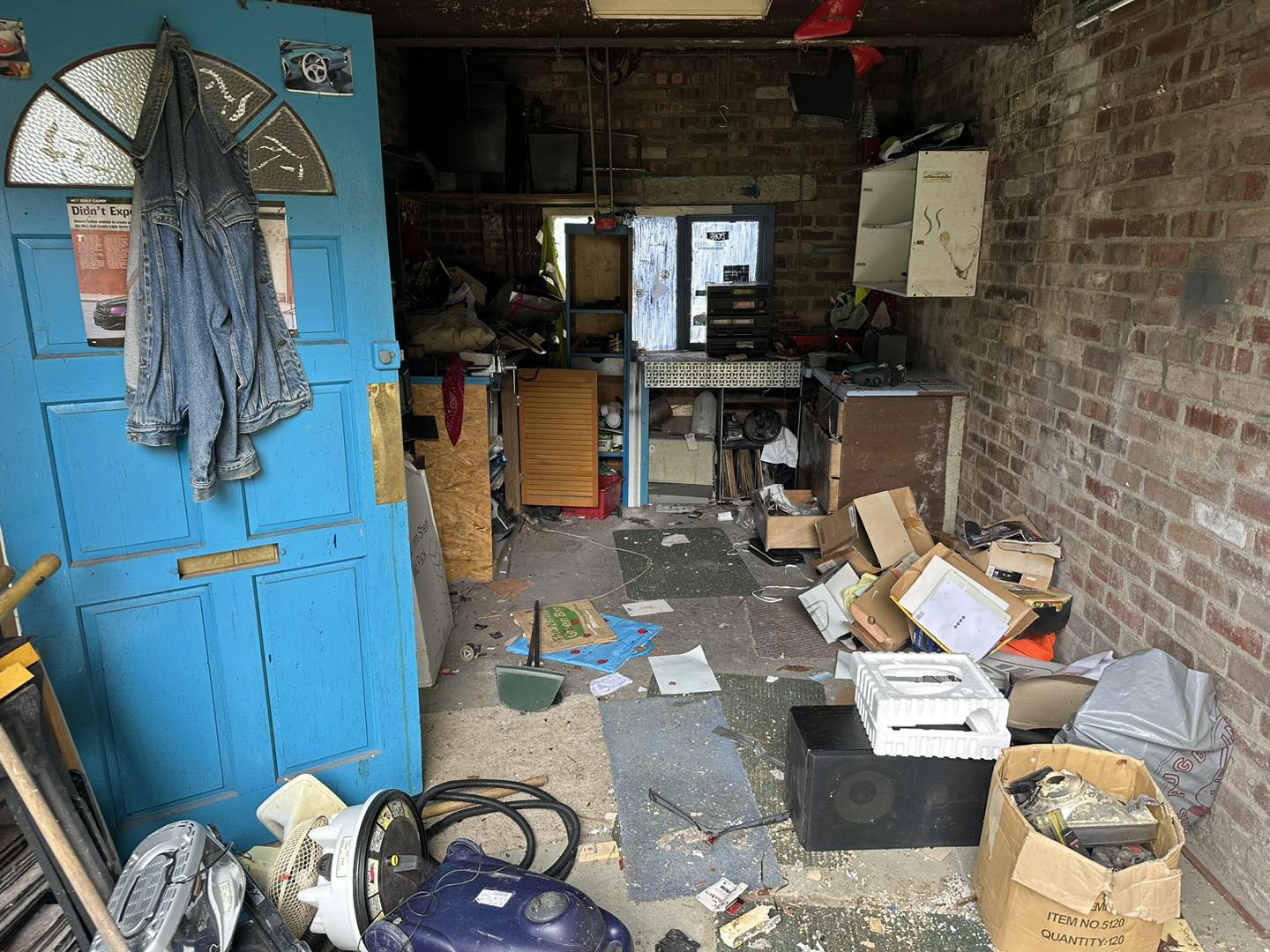 a photo of a garage room with a brick wall and a blue door. Waste all over the floor, and old tools in Neath, Port Talbot, and Swansea