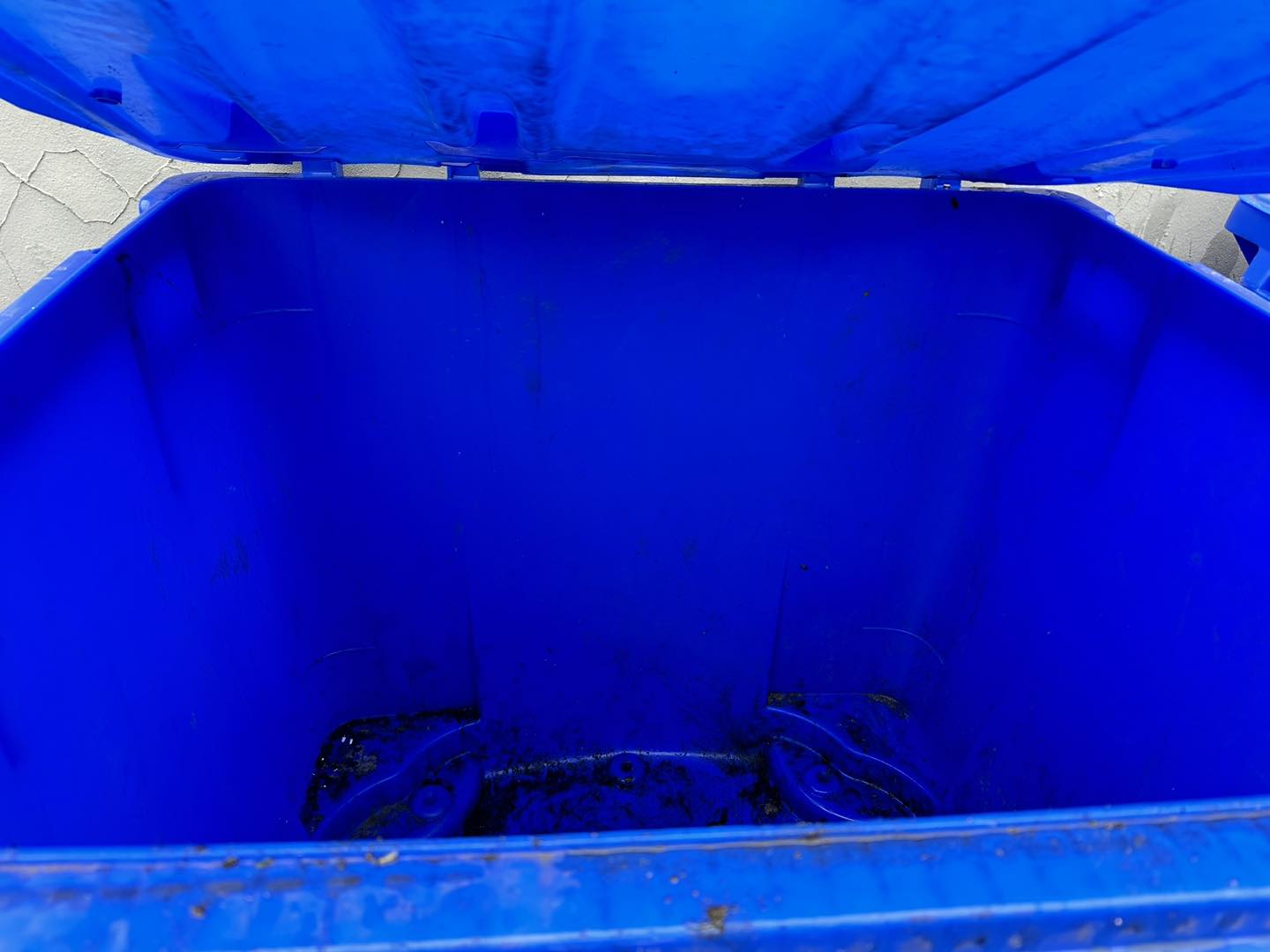 A clean outdoor area with a blue general waste bin and a green recycling bin on a gravel surface near a wooden fence and brick wall.